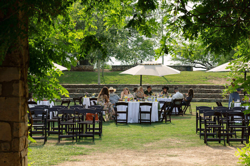 People sitting at round tables with white table cloths on grass inside the amphitheater at the san antonio botanical garden