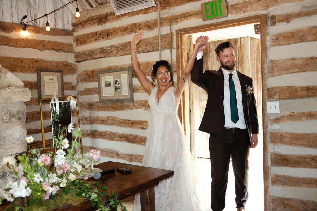 Bride and groom walking into their reception with hands in the air and smiles
