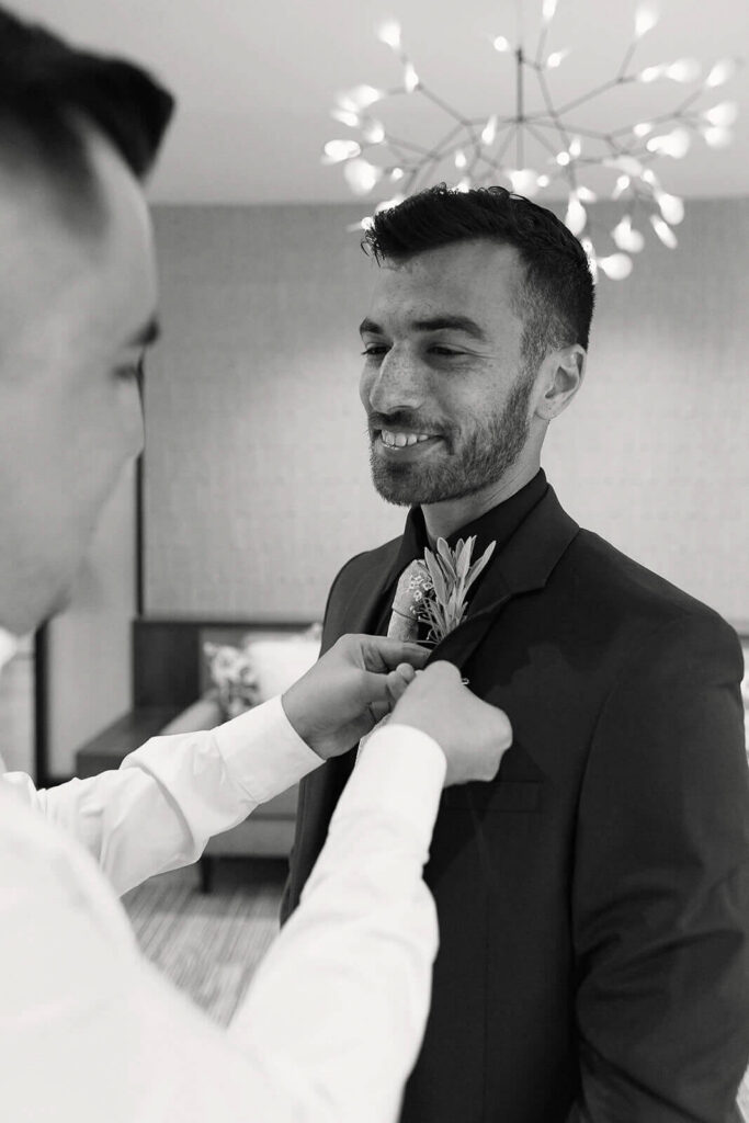 Two grooms help put on each others boutineers inside the getting ready room at Betty Kelso Center at The San Antonio Botanical Garden
