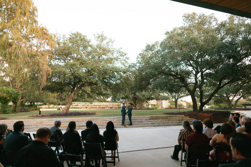 Two grooms standing on the steps in front of The Betty Kelso Center during their wedding at The San Antonio Botanical Garden. LGBTQ+