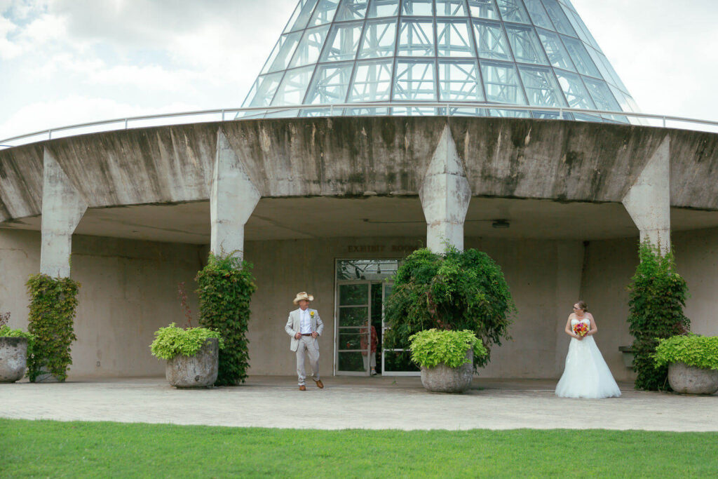 Bride and groom standing outside a biome at the botanical garden with concrete columns in between them