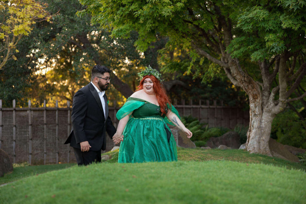Groom and bride in green fairytale dress walking through Japanese Garden surrounded by ornamental tree and rolling hills